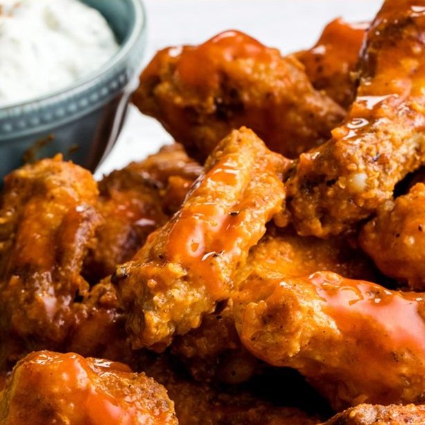 Frittierte Hähnchenflügel mit scharfer Sauce und einer Schüssel mit Dip.